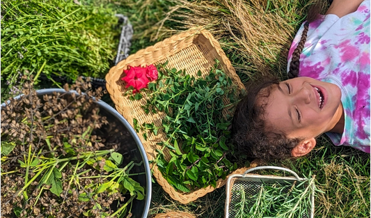girl laying in the grass with sage, rosemary, time, and rose surrounding her head like hair