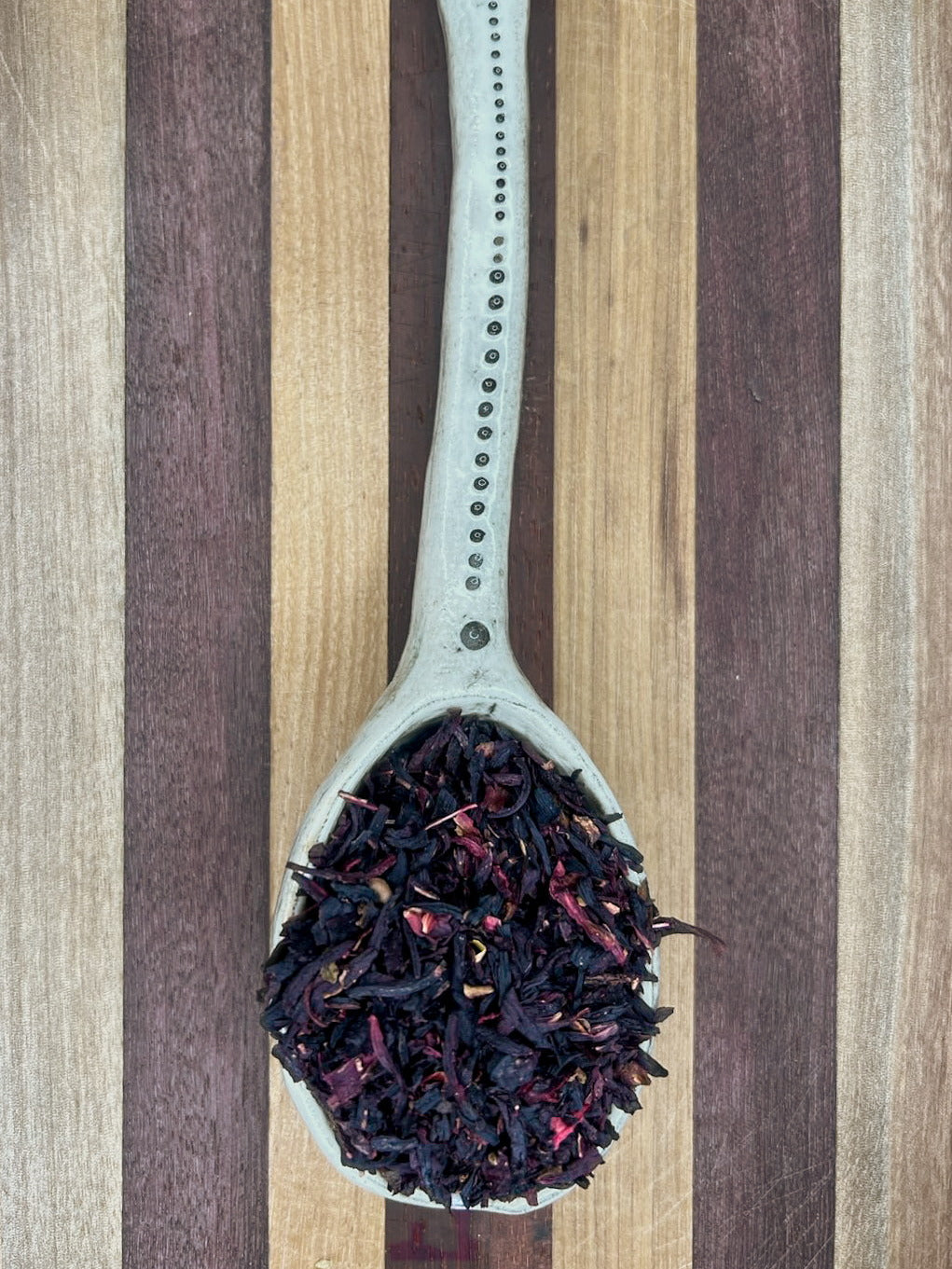 Pale blue spoon holding deep red dried hibiscus flowers on a striped wooden board