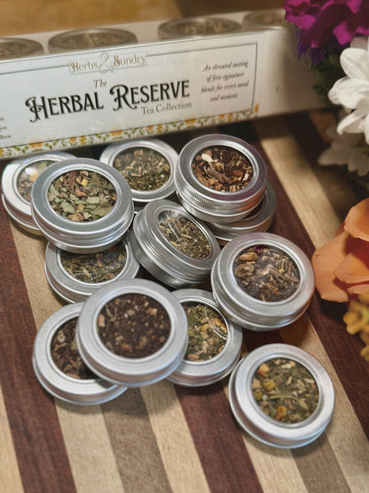 Open Herbal Reserve tins fanned across a striped wooden board, each holding a different loose leaf blend