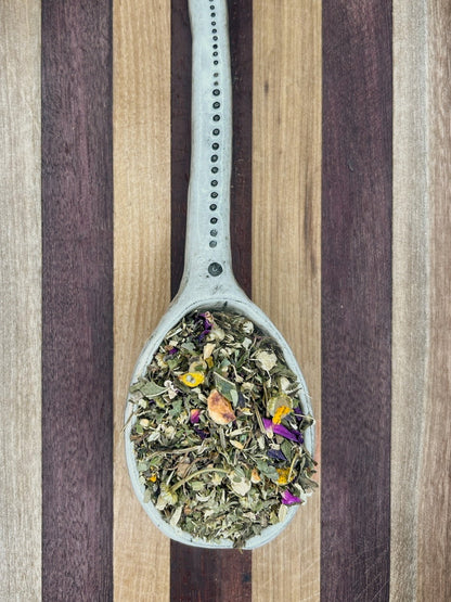 Pale blue spoon holding the green Relax and Digest loose leaf blend on a striped wooden board
